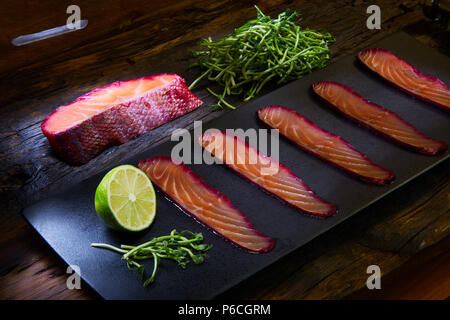 Sliced salmon fillet, salted with beetroot juice, served on whole wheat with salad leaves, sea salt and pepper over metal surface. Top view. Stock Photo