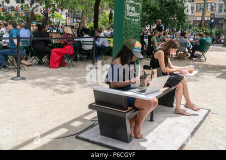 Workers in Madison Square Park in New York enjoy being outdoors at the L.L. Bean Outdoors' "Be an Outsider at Work" pop-up co-working space on Thursday June 21, 2018. Promoting an outdoor lifestyle and reacting to research that shows workers between the ages of 22-65 spend 95 percent of their time outdoors the outdoor goods retailer created their portable pop-up office complete with a complement of comfortable office furniture and wi-fi. The busy branding event attracted many people for meetings and just to work on their laptops and was lucky enough not to be on a day where New York's oppressi Stock Photo