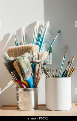 A bunch of different types of paint brushes placed in tin can on white wall background in sunny day Stock Photo