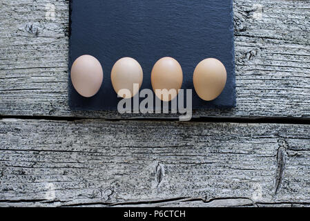 Five raw chicken eggs lie on a black board on a wooden background. Stock Photo