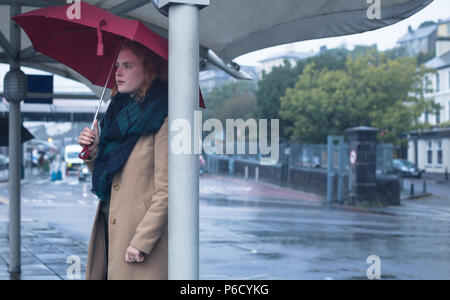 Young woman holding an umbrella standing at bus stop Stock Photo