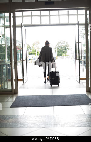 Woman with trolley bag leaving hotel Stock Photo