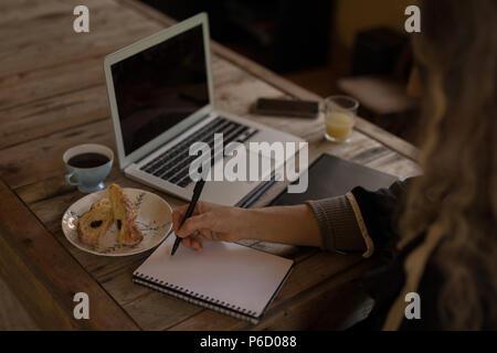 Mature woman sitting on chair and writing on note book Stock Photo