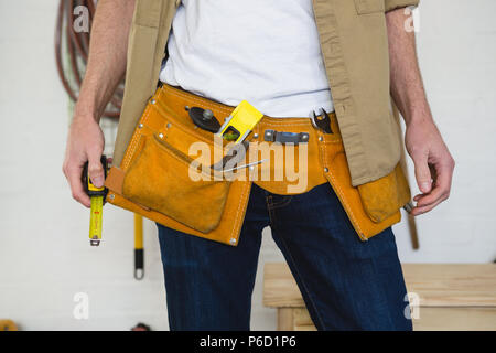 Male carpenter with tool belt in workshop Stock Photo
