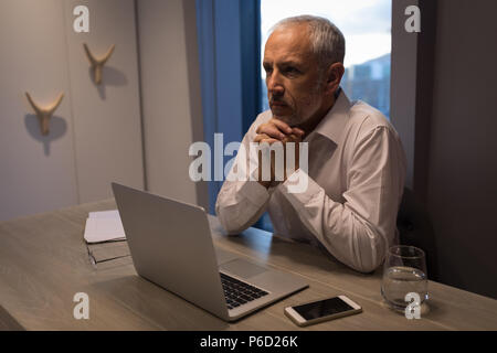 Businessman thinking deeply while sitting at desk Stock Photo