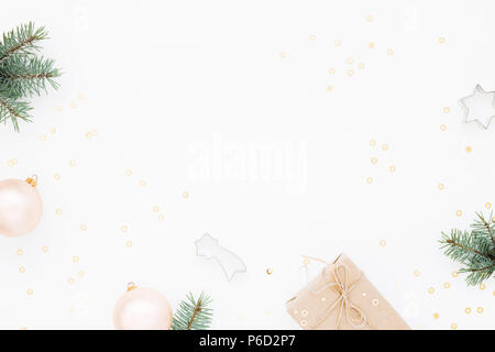 Minimal styled Christmas background with gift box, blush baubles, fir branches and baking molds on white. Holiday flat lay, top view. Stock Photo