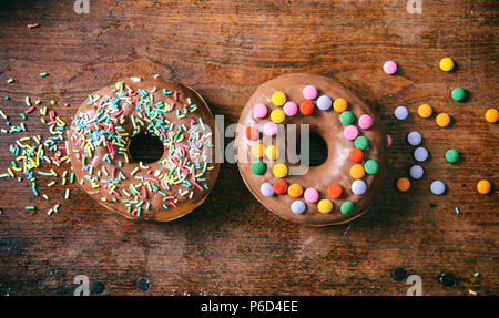 Pastries concept. Donuts with chocolate glaze, sprinkles , 2, top view and isolated on wooden background. Stock Photo