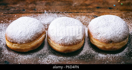 Jelly filled doughnuts concept. Krapfen with powder sugar, three and isolated on wooden background. Stock Photo