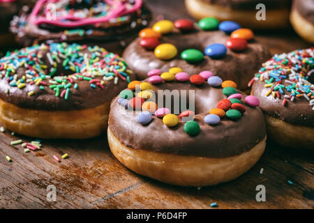 Pastries concept. Donuts with chocolate glaze and sprinkles, on wooden table blurry background. Stock Photo