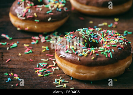Pastries concept. Donuts with chocolate glaze with sprinkles, on wooden table blurry background. Stock Photo