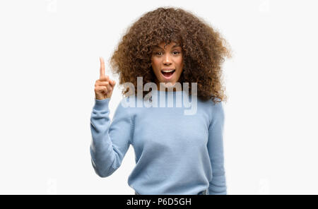 African american woman wearing a sweater pointing finger up with successful idea. Exited and happy. Number one. Stock Photo