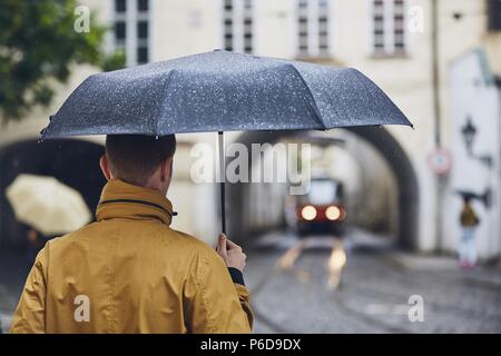 Young man holding umbrella walking in rain. Old city street in Prague, Czech Republic Stock Photo