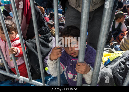 Refugee girl behind railings close to the gate as they wait to cross the border at the makeshift refugee camp of the Greek-Macedonian border near the  Stock Photo