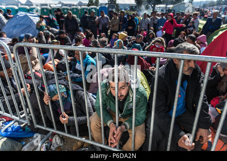 Refugee gather behind railings close to the gate as they wait to cross the border at the makeshift refugee camp of the Greek-Macedonian border near th Stock Photo