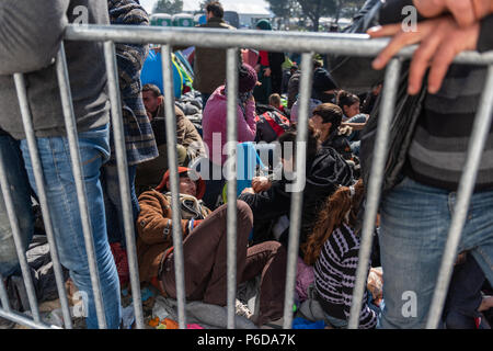 Refugee gather behind railings close to the gate as they wait to cross the border at the makeshift refugee camp of the Greek-Macedonian border near th Stock Photo