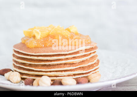 Stack of freshly backed pancakes on a vintage plate with nuts and orange jam on top. Front view. Copy space Stock Photo
