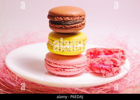 Brown, yellow and pink macaroons stack of pastel colors standing on a small white plate and pink decorative background. Front view. Stock Photo