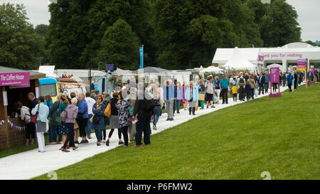 Large crowd of people at showground, walking near entrance, past trade stands & exhibits at busy RHS Chatsworth Flower Show, Derbyshire, England, UK. Stock Photo