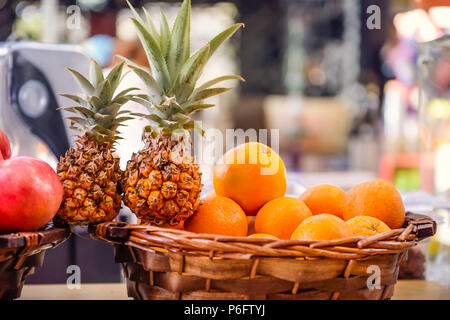 Fresh fruits for making juice - oranges in the basket, pineapples, pomegranates on the shop display on market place in Tel Aviv, Israel. Selective focus. Copy space. Stock Photo