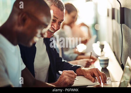 Young African designer and a mature colleague talking and laughing together while working in a modern office Stock Photo