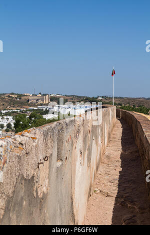 Detail of the fortification wall with a path and with portuguese flag. View on a city on the hill. Bright blue sky. Castro Marim, Algarve, Portugal. Stock Photo