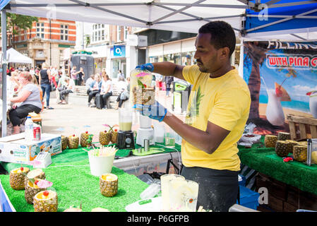 African ethnic preparing pina colada in pineapple on street - Food Street Market Reading, United Kingdom - June 2, 2018 Stock Photo