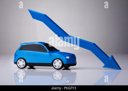 Declining Arrow Over Blue Car Against Gray Background Stock Photo