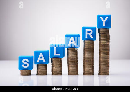 Blue Salary Cubic Blocks On Increasing Stacked Coins Against White Background Stock Photo