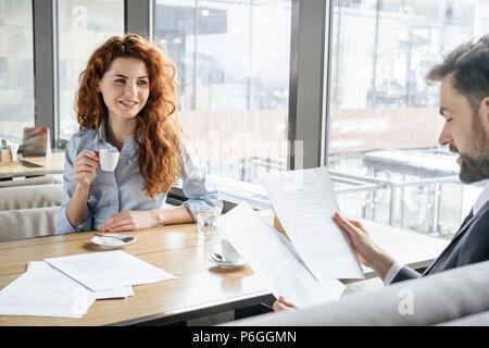 Man and woman having coffee break at restaurant sitting at table drinking hot coffee reading documents smiling cheerful Stock Photo