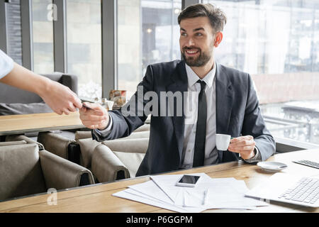 Businessman on business lunch at restaurant sitting at table giving credit card to waitress paying for coffee smiling happy Stock Photo