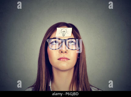 Young woman having sticker on face with symbol of light bulb and looking up thinking about solution Stock Photo