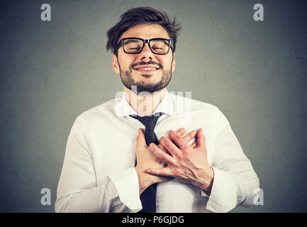 Man with eyes closed keeps hands on chest near heart, shows kindness, expresses sincere emotions, being kind hearted. Body language feelings concept Stock Photo