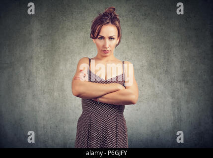 Young woman in dress holding hands crossed and looking at camera with anger and complaint on gray background Stock Photo