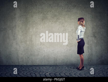 Side view of businesswoman standing in front of gray wall and contemplating in effort to solve problem Stock Photo