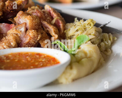 Crispy fried pork leg placed on a plate with vegetables and seasoning sauce Stock Photo