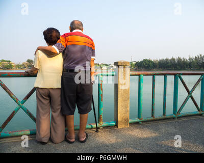 Happy romantic senior asian couple stand on the bridge in front of the lake. Husband stands with his wife. Concept of senior couple and take care of e Stock Photo