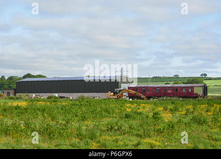 The Caledonian Railway Sidings at Bridge of Dun in Angus, Scotland. With An old Railway carriage and Excavator in a Field next to the Station. Stock Photo