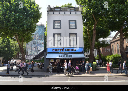 People walk past a branch of the coffee shop, Caffé Nero on Tottenham Court Road, central London where people are drinking coffee seated on outside ta Stock Photo