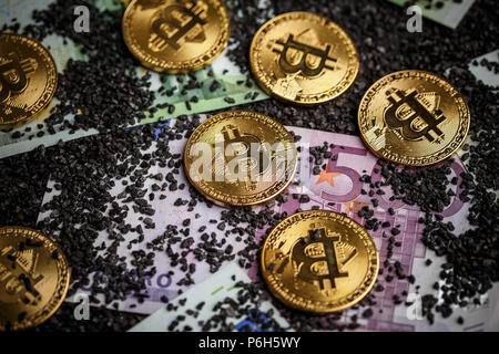 Golden bitcoins on euro banknotes and small black coal background Stock Photo