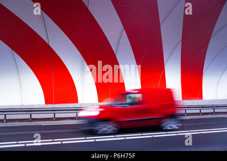 A red car driving fast in a tunnel with red dynamic stripes on the wall. Stock Photo