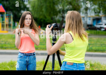 Two teenage girls. In the summer in the city. Writes the video to the camera. Concepts of young bloggers and bloggers. In the hands holds the phone. Stock Photo