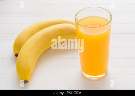 Glass of multifruit juice and two bananas on a white wooden table.Tropical healthy breakfast. Stock Photo