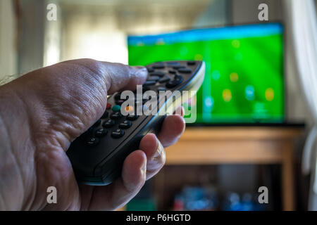 closeup of male hand uses the remote control during a football game on TV Stock Photo