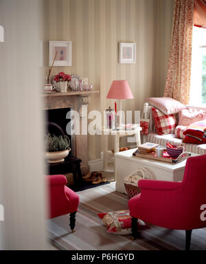 Deep ink armchairs and white painted chest used as a coffee table in sitting room with striped wallpaper and a pale pink lamp Stock Photo