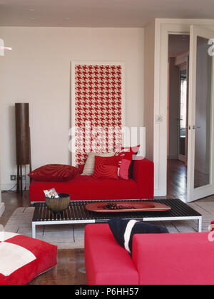 Patterned red cushions on bright red sofa in front of large red+white hounds-tooth picture in living room with black coffee-table Stock Photo