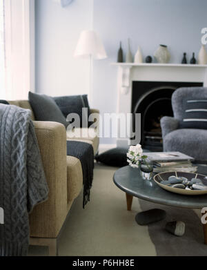 Grey knitted throw on beige sofa in pale grey living room with traditional fireplace and modern coffee-table Stock Photo