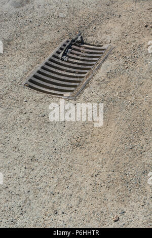 Drainage grille on a country lane. Metaphor 'down the drain'. Stock Photo
