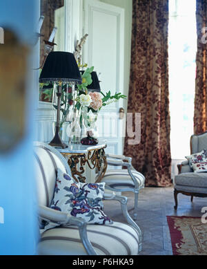 Floral cushions on striped French-style chairs in townhouse drawing room with brown patterned cut-velvet curtains Stock Photo