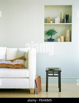 White sofa and small black stool in modern living room with Bonsai tree and collection of vases on alcove shelving Stock Photo