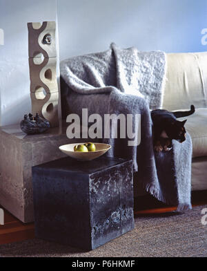 Close-up of oblong concrete lamp on cube table beside sofa with cat on grey mohairl throw in modern living room